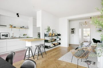 aménager-une-petite-cuisine-semi-ouverte-blanche-avec-petit-bar-salon-avec-parquet-chaises-scandinaves-canapé-blanc-cassé-tapis-gris-étagère-noire